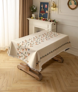 Close-up of Christmas reindeer tablecloth with white pom-pom tassels and pine tree patterns