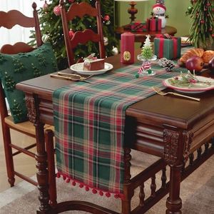 Christmas plaid table runner with red pompoms on a wooden table with festive decor