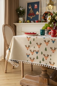 Detail of Christmas tablecloth with orange reindeer pattern and white pom-pom tassels
