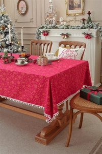 Close-up of red Christmas tablecloth with gold bell patterns and white pom-pom trim