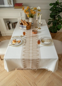 Close-up of beige jacquard tablecloth with vintage patterns and elegant white fringe