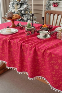 Close-up of red Christmas tablecloth with gold bells, snowflakes and white pom-pom fringe
