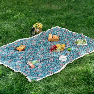 Navy floral jacquard picnic blanket with white decorative fringe on outdoor lawn