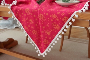 Detail of red Christmas tablecloth with golden bells and white pom-pom fringe trim