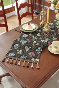 Détail d'un chemin de table vintage en jacquard floral avec glands colorés sur bois