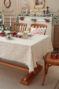 Detail of Christmas tablecloth with gold bells, snowflake prints and white pom-pom trim