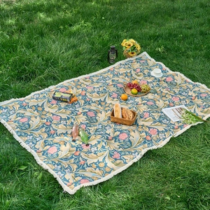 Blue jacquard picnic mat with vintage flower patterns and white tassels on green grass