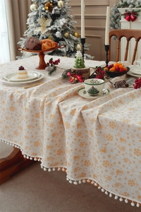 Detail of Christmas tablecloth with gold bell patterns and white pom-pom tassel fringe