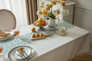 Close-up of geometric jacquard tablecloth with beige tassels and green leaf patterns