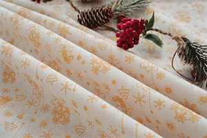 Detailed close-up of beige Christmas tablecloth featuring orange bell and snowflake prints