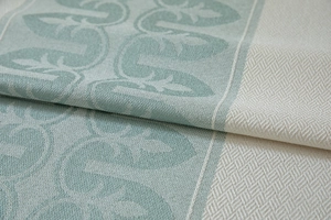 Detailed macro view of sage green jacquard fabric with large leaf patterns and fringe