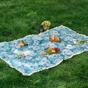 Blue daisy pattern jacquard picnic mat with white tassels displayed on green grass