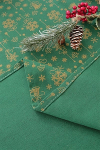 Close-up of green Christmas tablecloth with gold festive bells and pine cone decor
