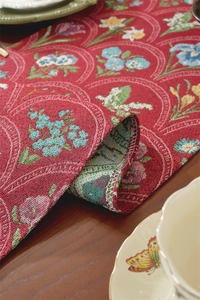 Détail du chemin de table jacquard rouge vintage avec motifs floraux et franges