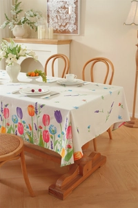 Detail of floral rectangular tablecloth with tulip print and tassels on a wooden table