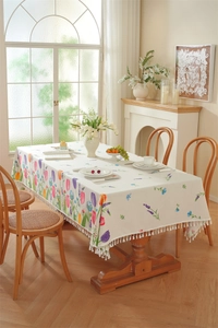 Detail of floral tulip print tablecloth with elegant white fringe on a wooden table