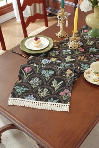 Détail d'un chemin de table jacquard floral avec glands blancs sur une table en bois vintage