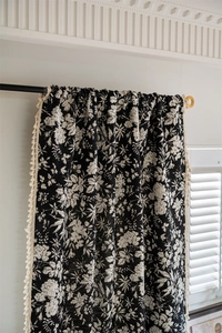 Detail of bohemian jacquard curtain featuring black floral patterns and cream tassels