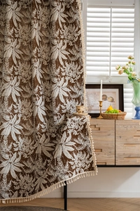 Detail of boho curtain featuring tropical leaf patterns and off-white tassel fringe