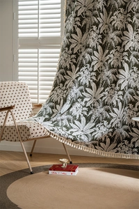 Close-up of tropical palm leaf pattern and cream tassel fringe on a green curtain