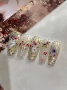 Detail of hand-painted floral press-on nails with embossed gold edges and matte finish