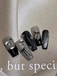 Dettaglio di unghie finte fatte a mano con effetto cat-eye nero, fiocchi e strass eleganti