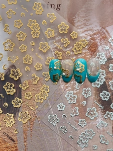 Detailed view of gold embossed cherry blossom nail art stickers on blue and matte nails