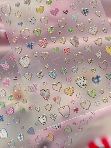 Macro shot of silver-stamped heart nail art stickers with elegant gold edges and plaid patterns