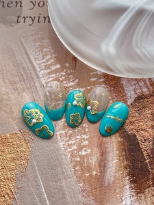 Close-up of blue marble press-on nails with 3D gold floral accents and mini pearls