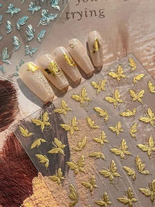 Dettaglio di adesivi 3D farfalla dorati e iridescenti per nail art su manicure nude