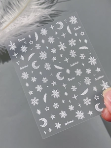 Macro view of 3D embossed snowflake and feather nail art stickers in white and silver