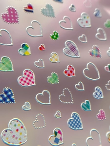 Macro shot of 3D embossed heart nail stickers with metallic silver edges and plaid patterns
