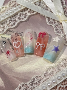 Détail de faux ongles style Coquette avec coeurs 3D, noeuds et étoiles sur de la dentelle