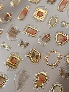 Macro detail of gold embossed 3D nail art stickers with heart and vintage frame designs