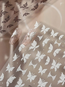 Macro view of 3D embossed white butterfly nail stickers with elegant linear floral patterns