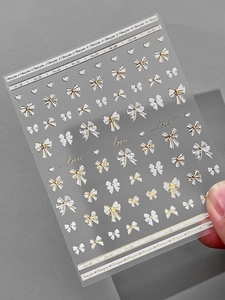 Macro detail of 5D embossed nail art stickers with white bows and hearts on grey background