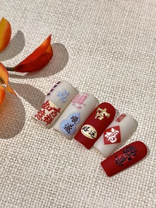 Macro detail of red and cream press-on nails with embossed golden Chinese characters