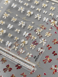 Macro shot of 3D embossed nail art stickers with red bows, gold hearts and love scripts