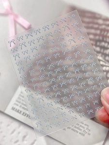 Macro shot of 3D silver bow nail art stickers with embossed jelly texture details