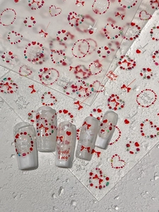 Détail de stickers nail art 3D avec cœurs rouges et nœuds sur capsules blanches