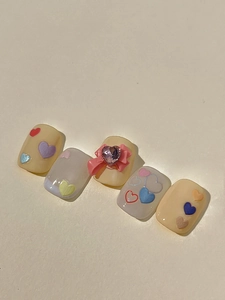 Détail macro de faux ongles jaune crème avec nœuds 3D et gemmes en forme de cœur