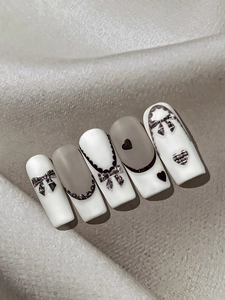 Détail de faux ongles trapèze mats avec nœuds en tweed et motifs de cœurs élégants