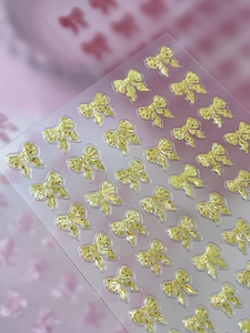 Macro view of 3D golden bow nail stickers with glitter finish and textured details
