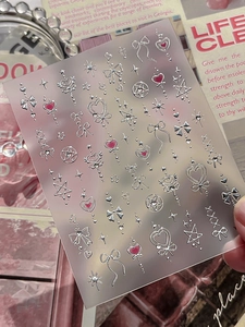 Macro view of 3D metallic silver bow and heart nail art stickers on matte backing