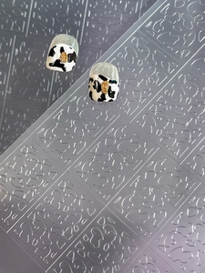 Macro shot of black and white cow print nail stickers with 3D gold metal accents