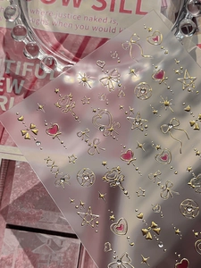 Macro detail of gold foil heart nail stickers with pink accents and sparkling rhinestones