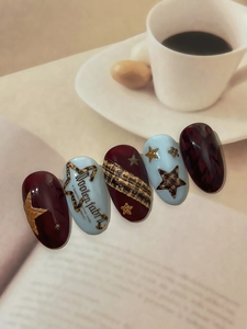 Detail of tweed texture nail art stickers with star motifs and deep burgundy tones