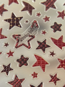 Macro detail of 3D star nail stickers with textured red and black woolen fabric patterns