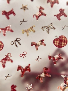 Detail of festive nail stickers featuring plaid terrier, red apples and gold glitter stars