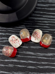 Detail of red and white press-on nails with gold firework patterns and silver stars